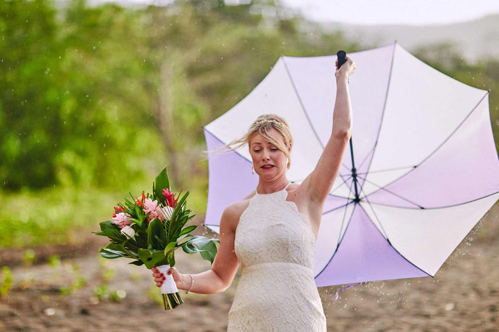 A bride laughing while holding an umbrella during a tropical rain shower on her wedding day in Costa Rica.