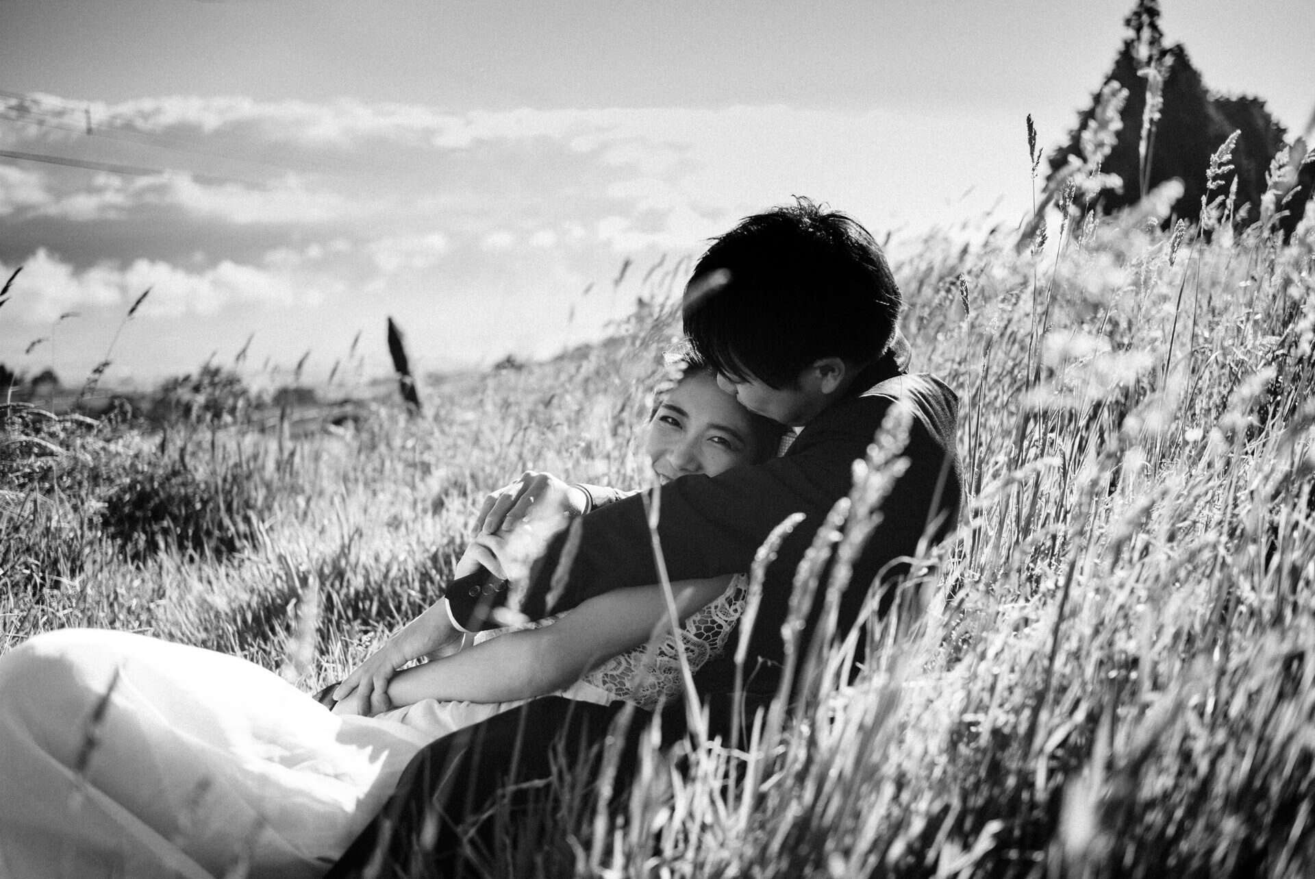 Bride smiling while embracing her partner in a grassy field during an intimate wedding portrait.